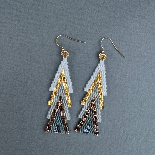 Beaded holiday earrings arranged flat, showing pine-inspired layers in white, gold, and bronze.”