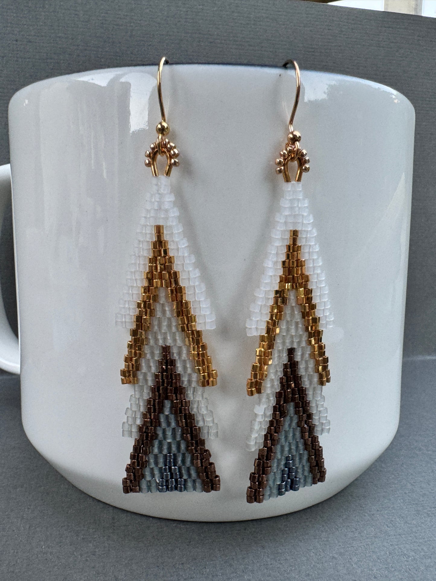 Close-up of beaded tree-shaped earrings showing layered white and metallic beads with gold-plated hooks.