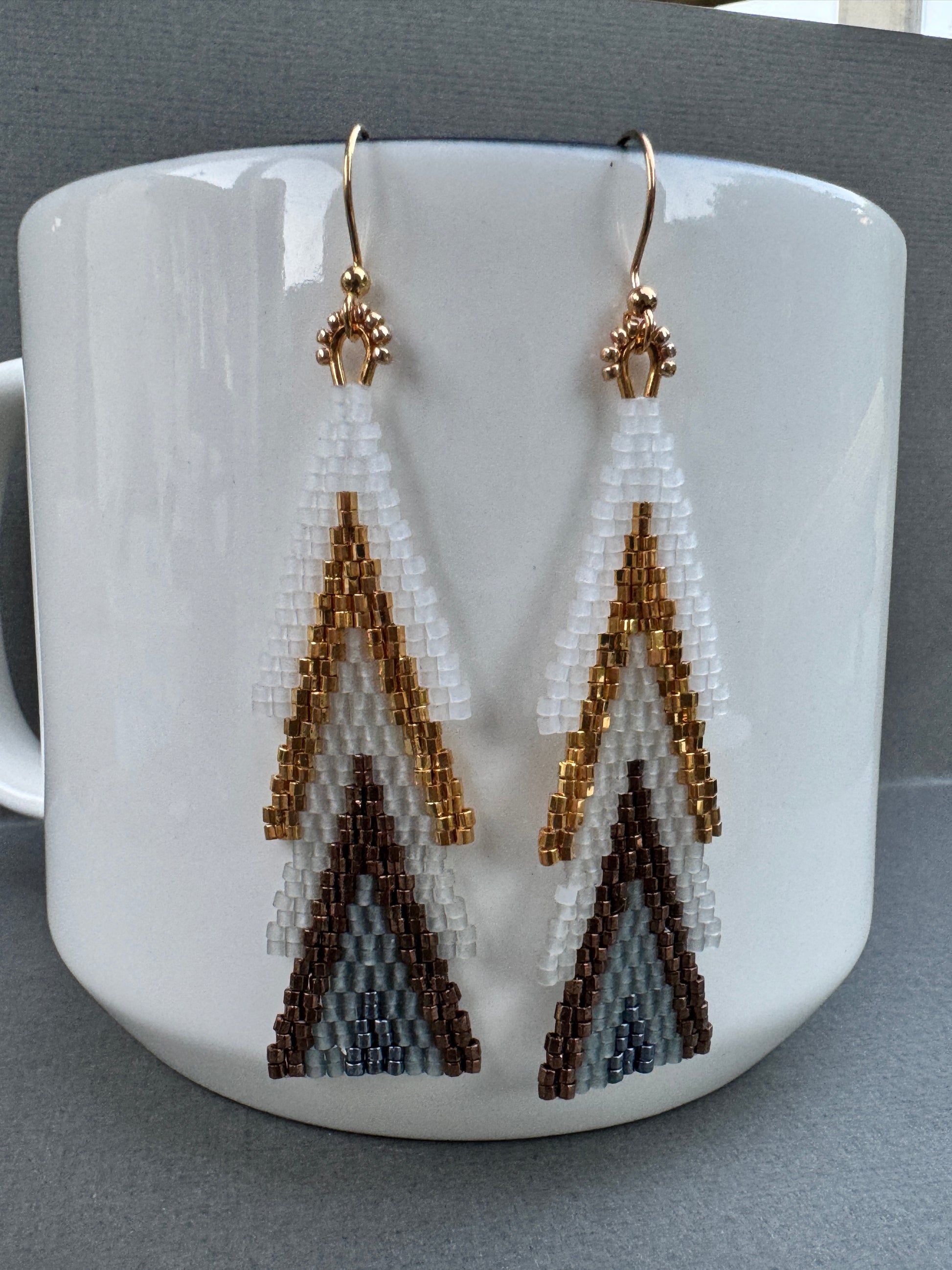 Close-up of beaded tree-shaped earrings showing layered white and metallic beads with gold-plated hooks.