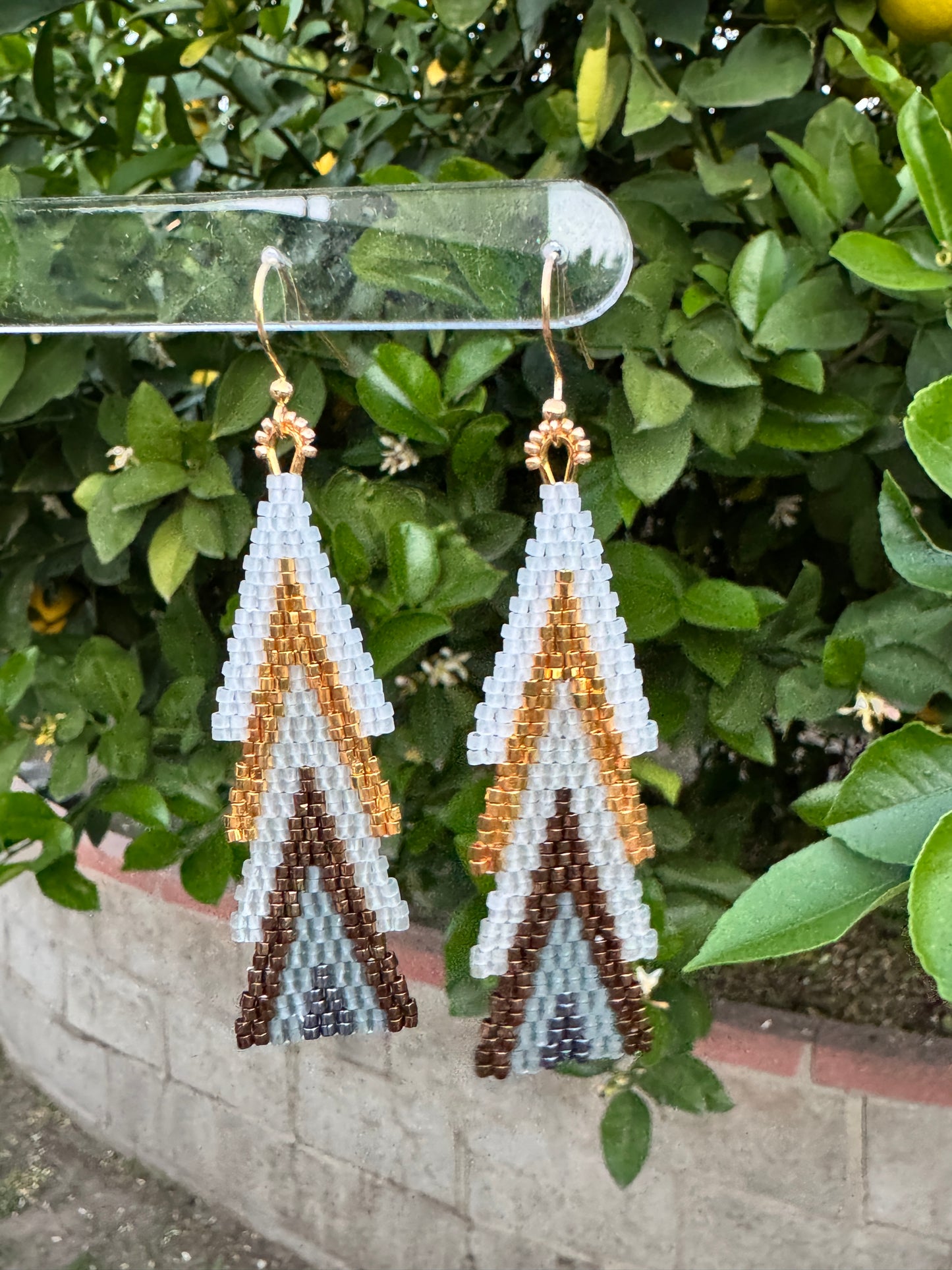 Hand-beaded earrings in a stacked pine-tree shape with white, gold, bronze, and grey seed beads and 24K gold-plated ear wires.