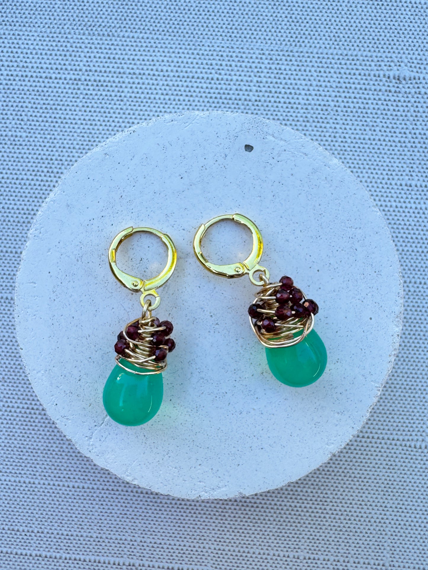 Green opal Czech glass drop earrings wrapped in gold-plated wire with garnet gemstone accents on gold huggie hoops.