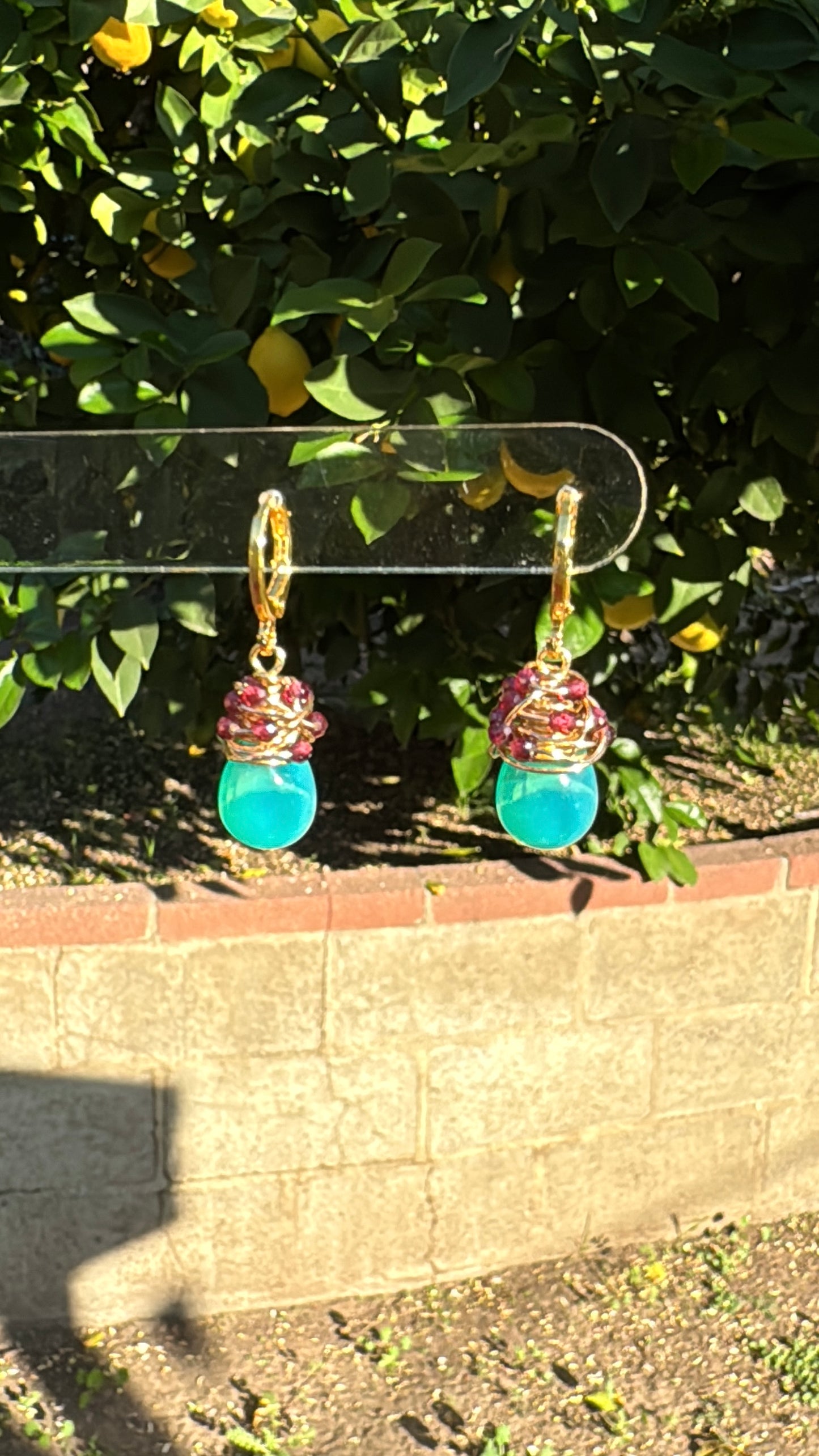 Handmade green opal drop earrings with garnet accents on gold-plated huggie hoops hanging outdoors.