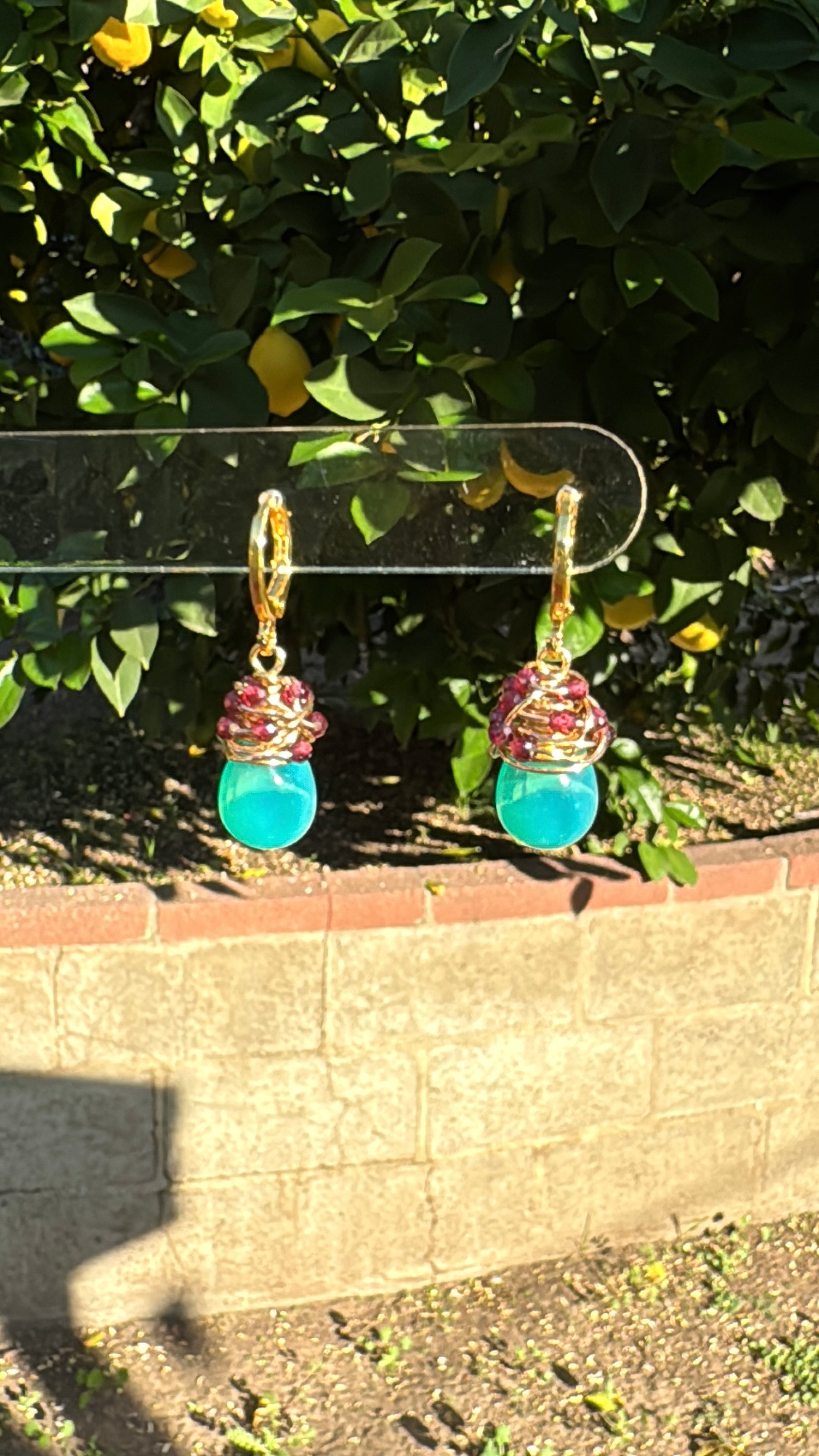 Handmade green opal drop earrings with garnet accents on gold-plated huggie hoops hanging outdoors.